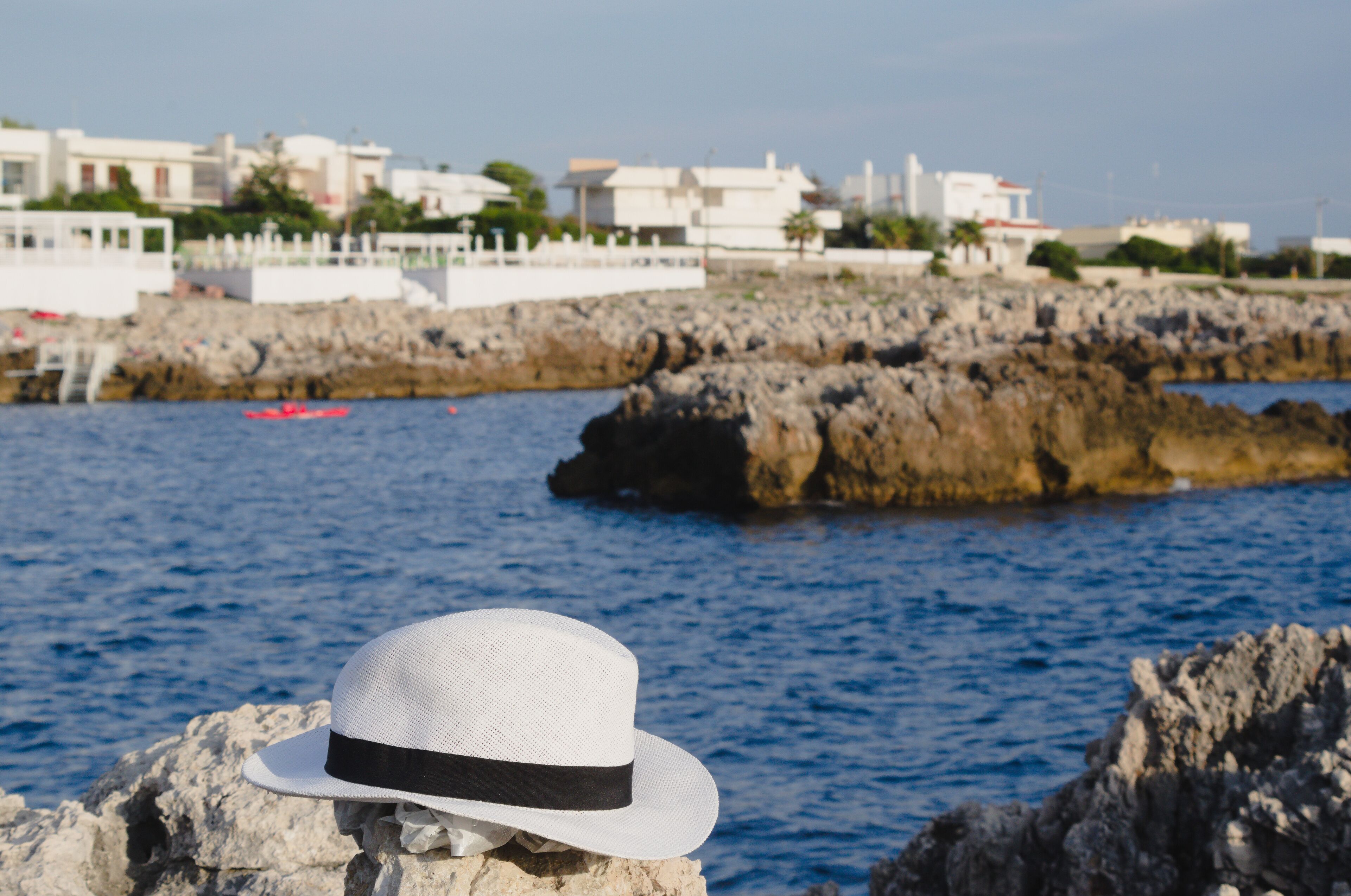 A white hat on a rock by the sea with buildings in the background.