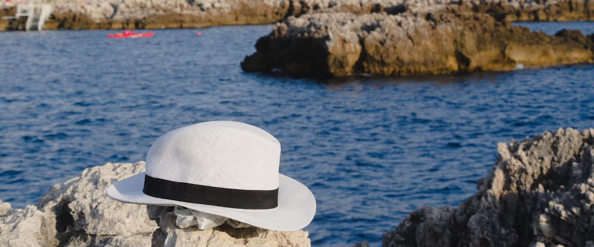 A white hat on a rock by the sea with buildings in the background.