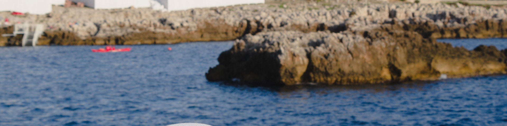 A white hat on a rock by the sea with buildings in the background.