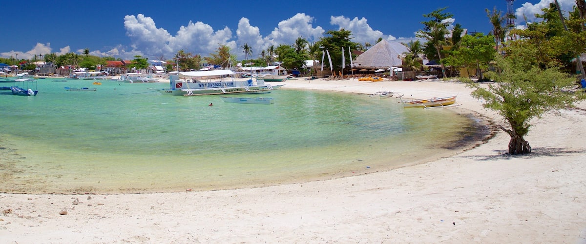 A beach with clear turquoise water, boats, and palm trees.