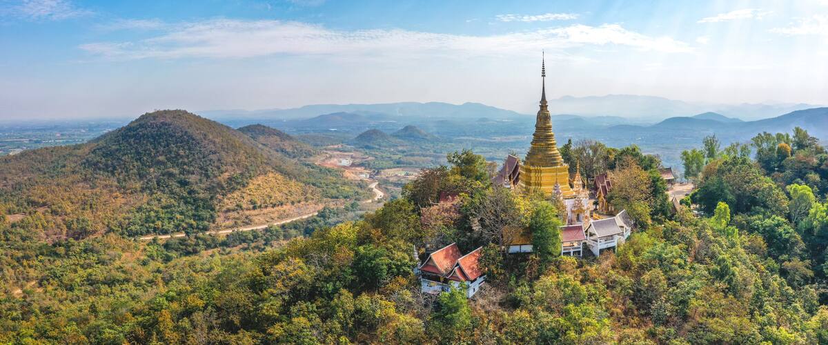 A temple complex on a hill with a winding road and surrounding forest.