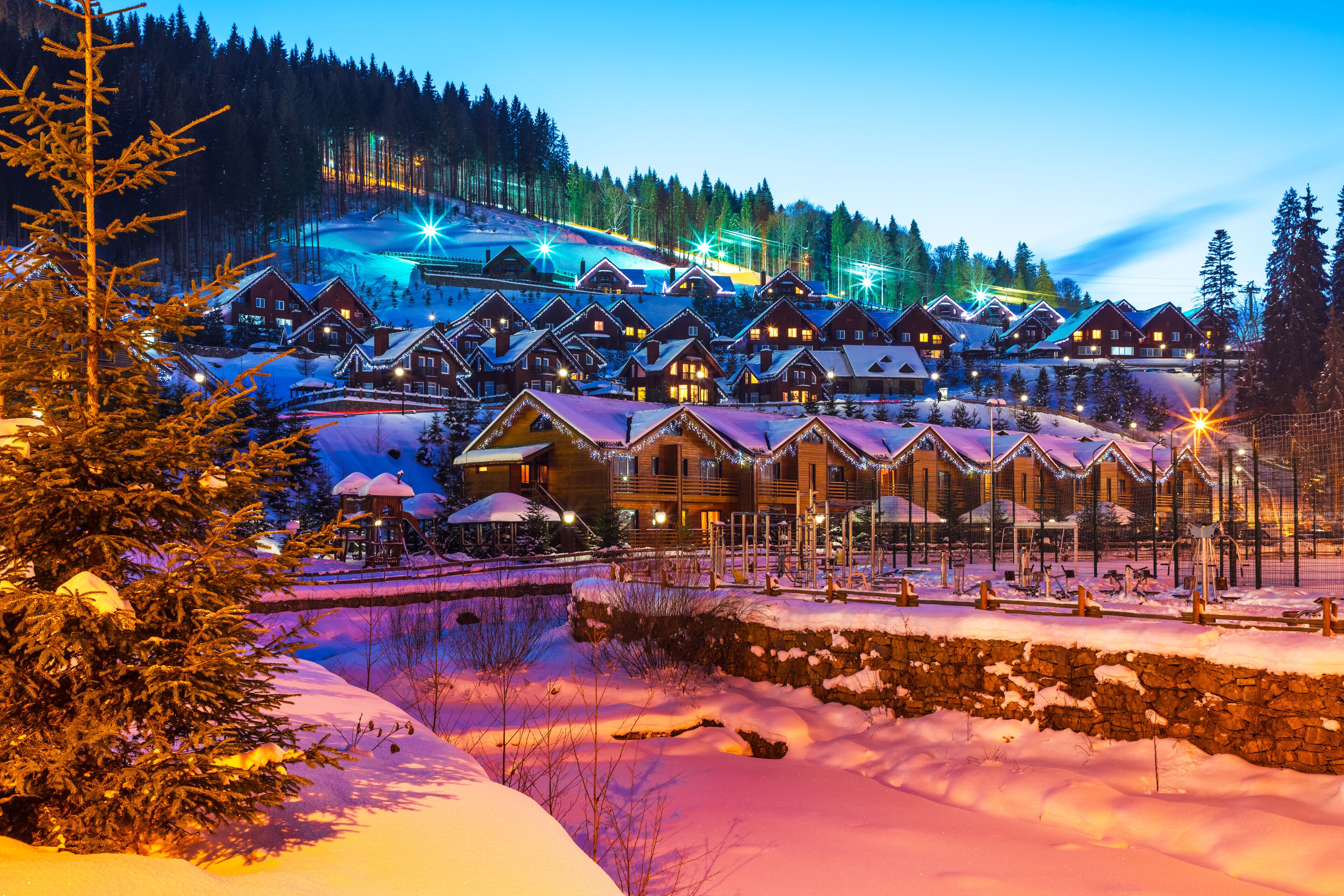 A snow-covered village with wooden houses and a ski slope in the background.