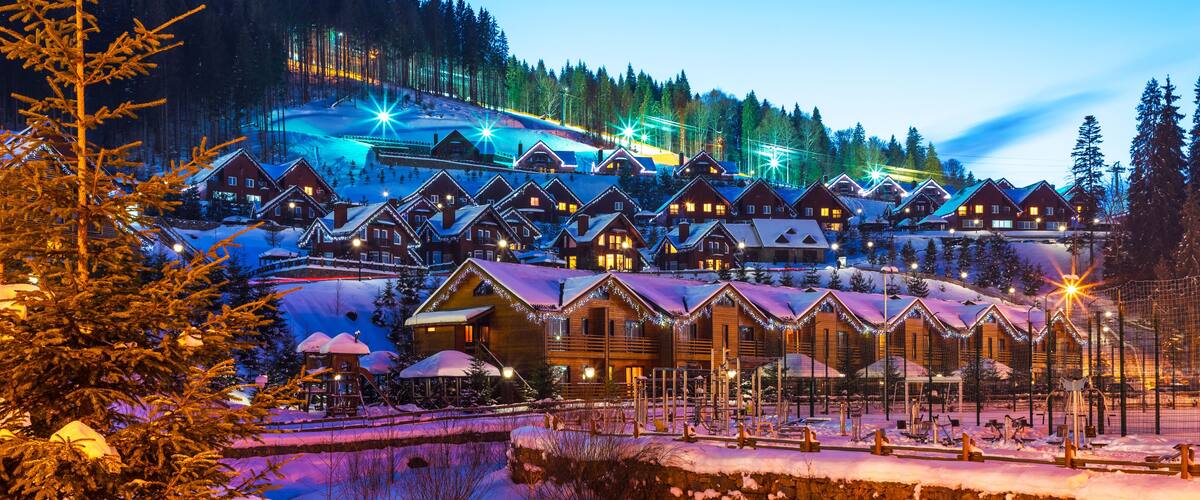 A snow-covered village with wooden houses and a ski slope in the background.