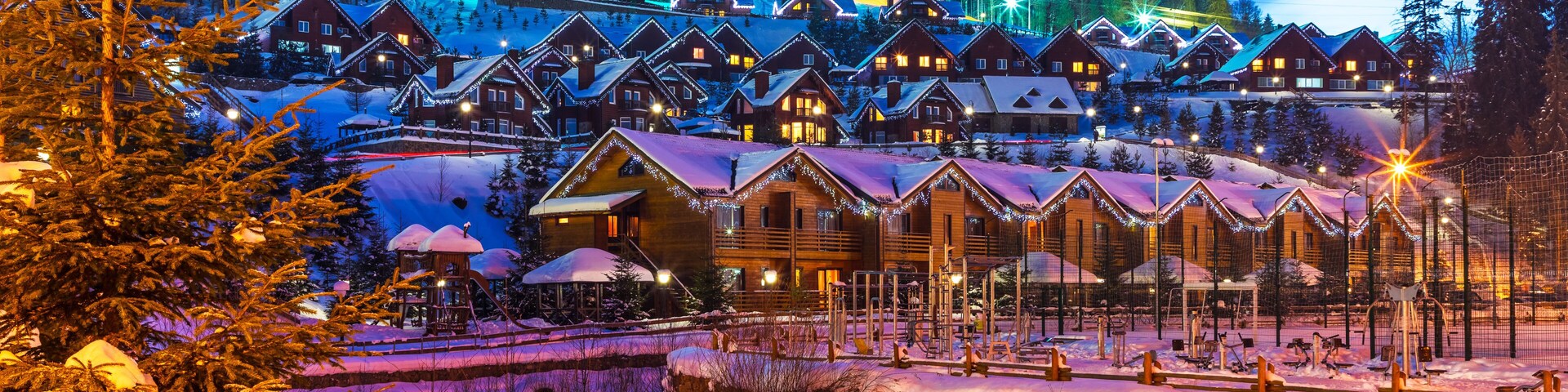 A snow-covered village with wooden houses and a ski slope in the background.