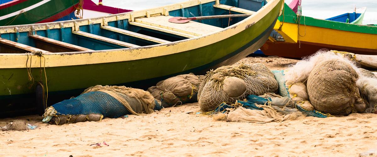 A row of colorful boats on a sandy beach with fishing nets and ropes.