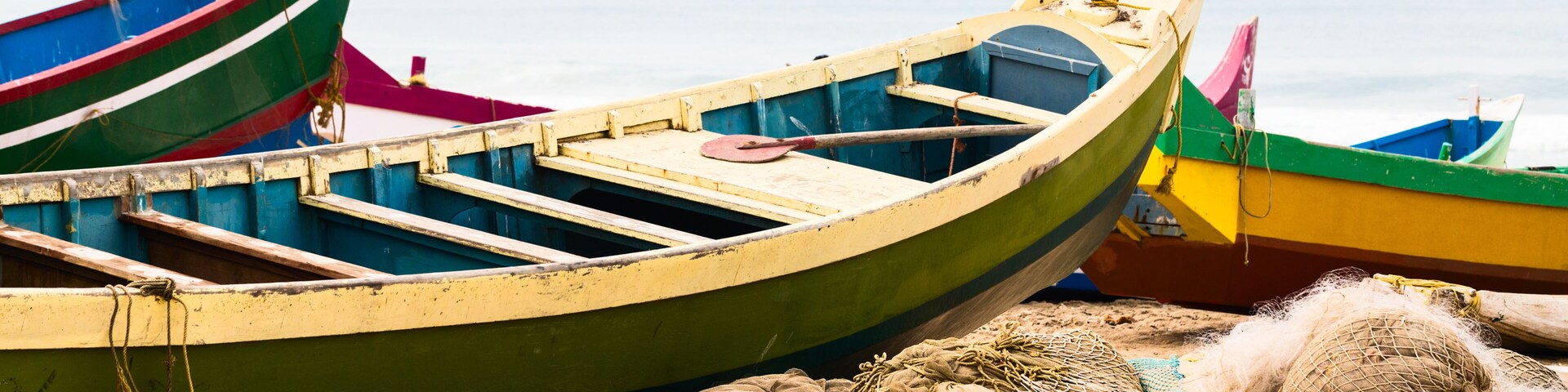 A row of colorful boats on a sandy beach with fishing nets and ropes.