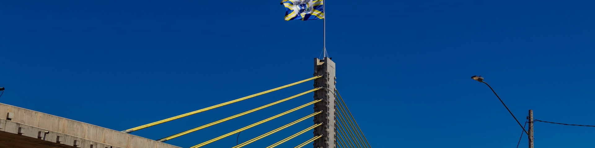 Viaduto Estaiado na cidade de Anápolis em Goiás. Viaduto com uma bandeira da cidade de Anápolis com céu azul ao fundo.