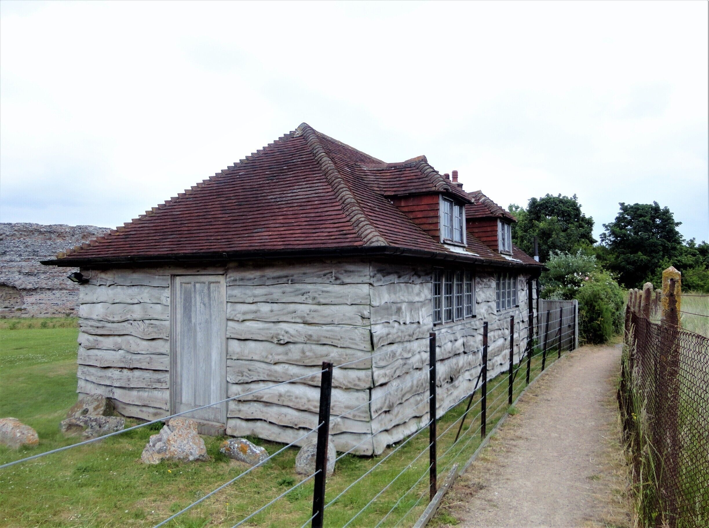 A stone building with a red-tiled roof, surrounded by a fence and a dirt path.