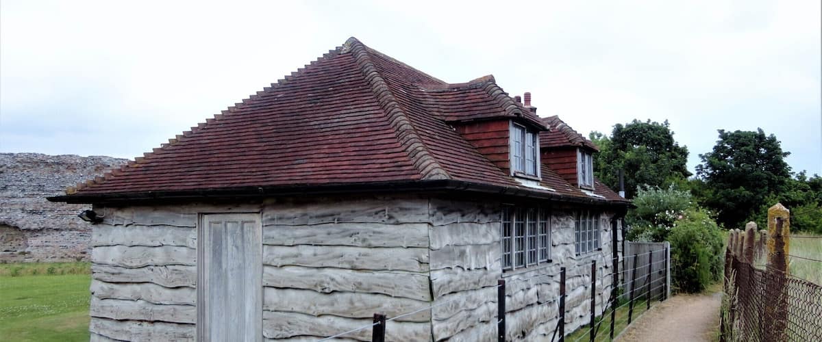 A stone building with a red-tiled roof, surrounded by a fence and a dirt path.