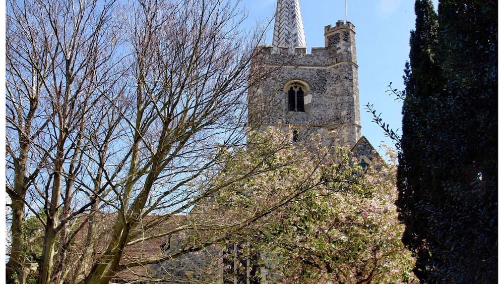Une église dotée d’un clocher élancé et surmontée d’un drapeau, entourée de pierres tombales dans un cimetière.