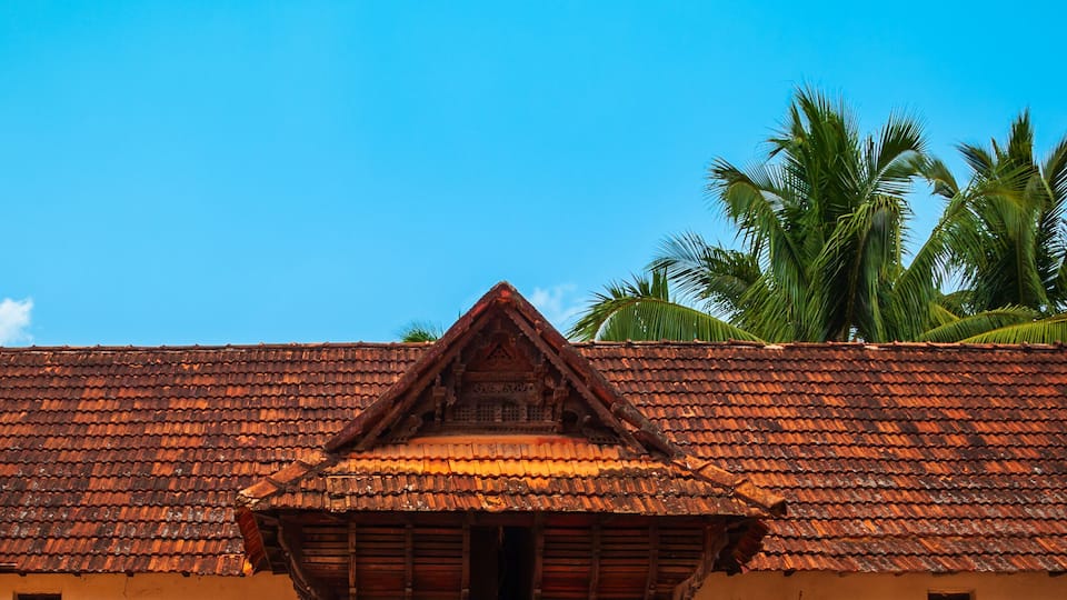 A traditional building with a tiled roof, a wooden entrance with intricate carvings, and two stone statues on either side.