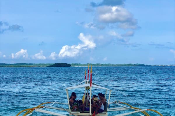 A boat with passengers on a calm sea, anchored near a sandy beach with distant islands.