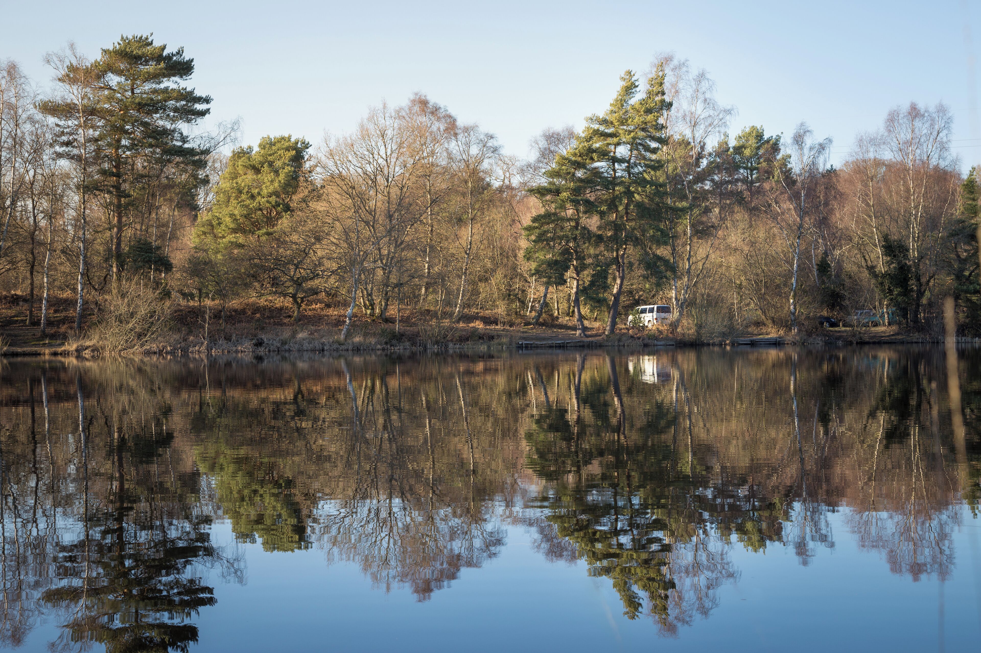 A calm lake with reflections of trees and a vehicle.