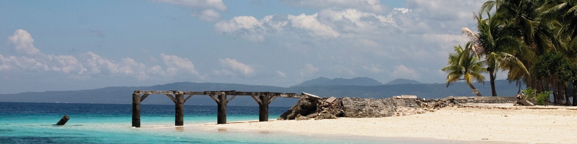 Damaged wooden wharf on a deserted tropical island with white sandy coral beach.