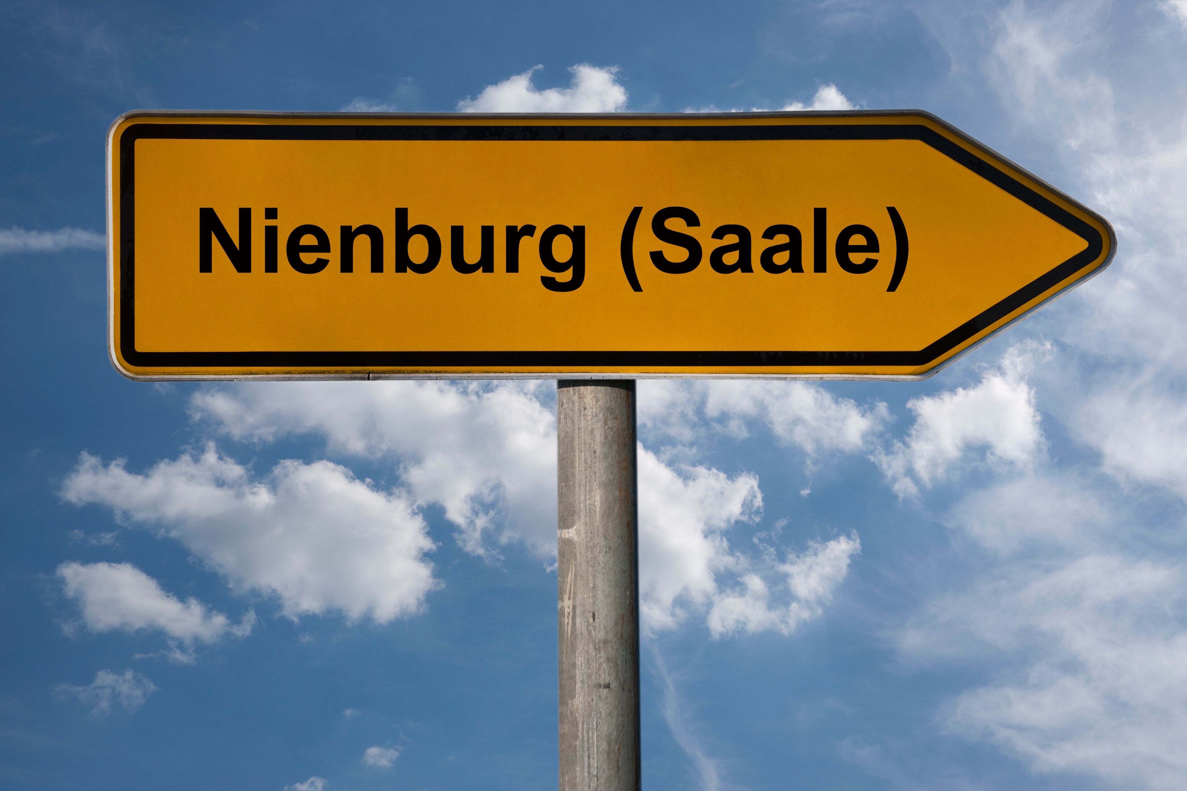 A directional sign pointing to Nienburg (Saale) against a blue sky with clouds.
