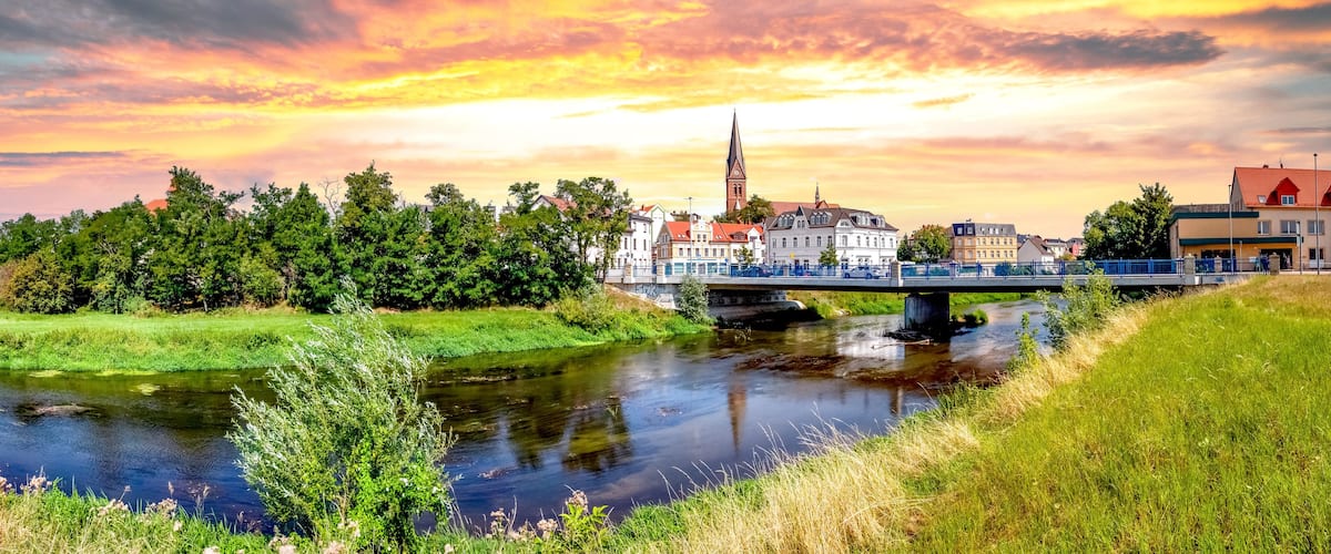 Ein Fluss mit einer Brücke, einer Kirche und einer Stadt mit Gebäuden.