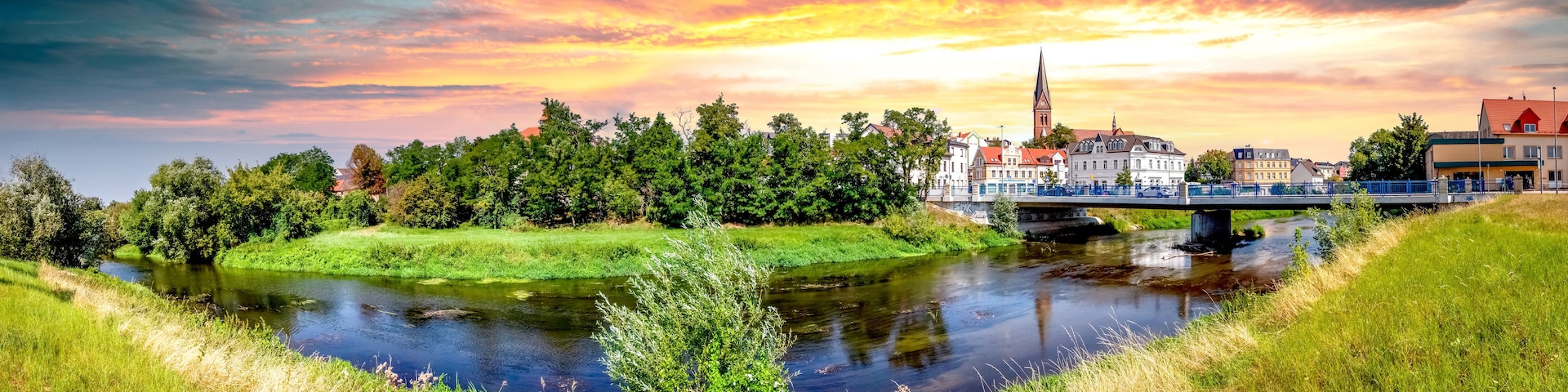A river with a bridge, a church, and a town with buildings.