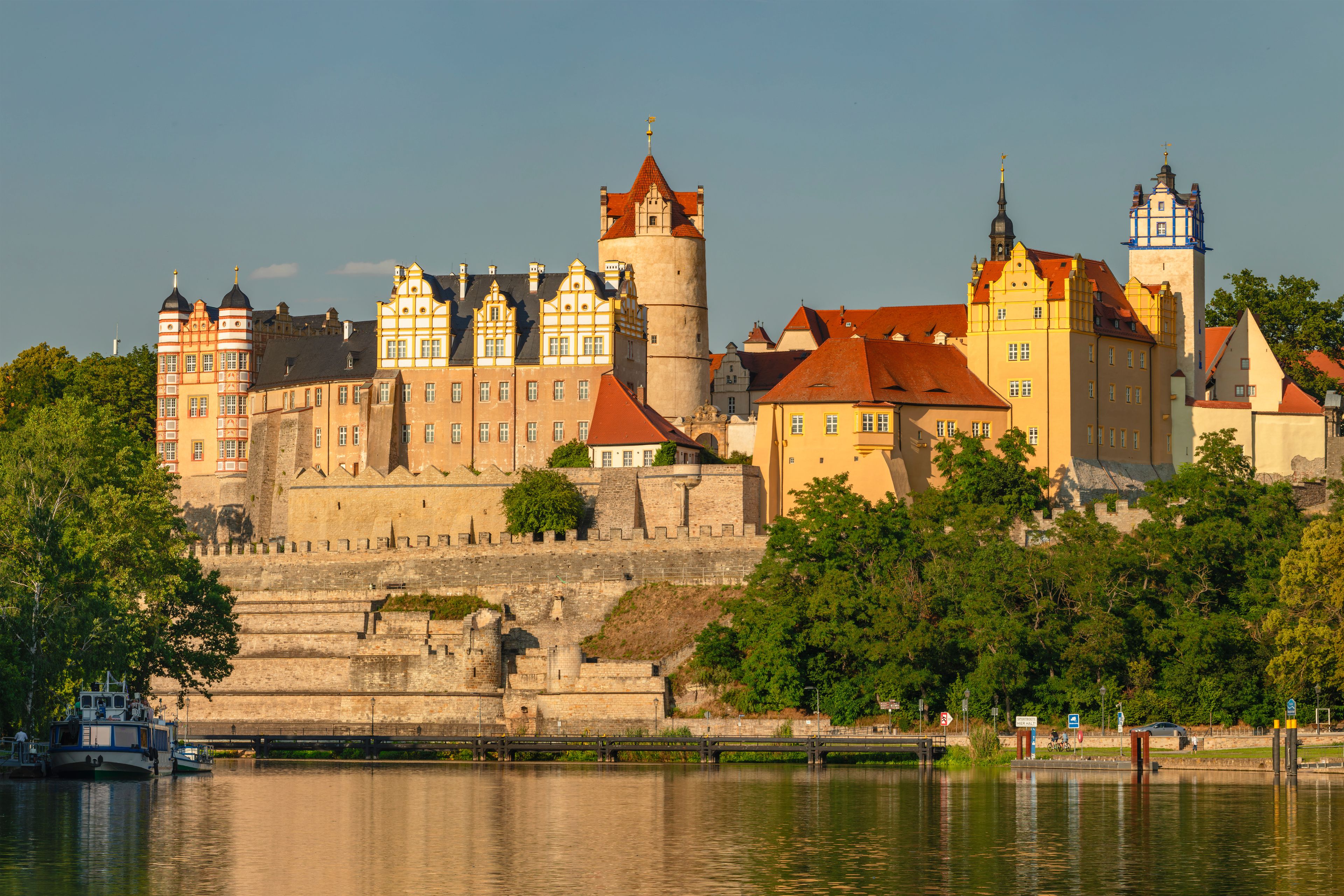 Eine historische Burg mit mehreren Türmen und einem Fluss im Vordergrund.