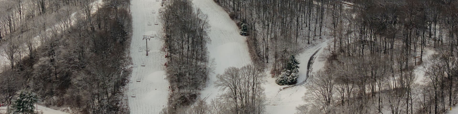 A snow-covered ski slope with ski lifts and trees.