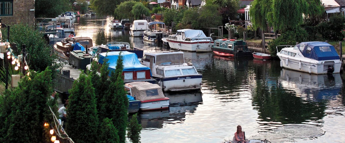 A canal with boats docked along the sides, surrounded by trees and buildings.