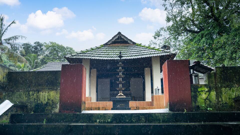 A traditional Japanese pagoda with a tiled roof, surrounded by lush greenery and a stone staircase leading up to it.