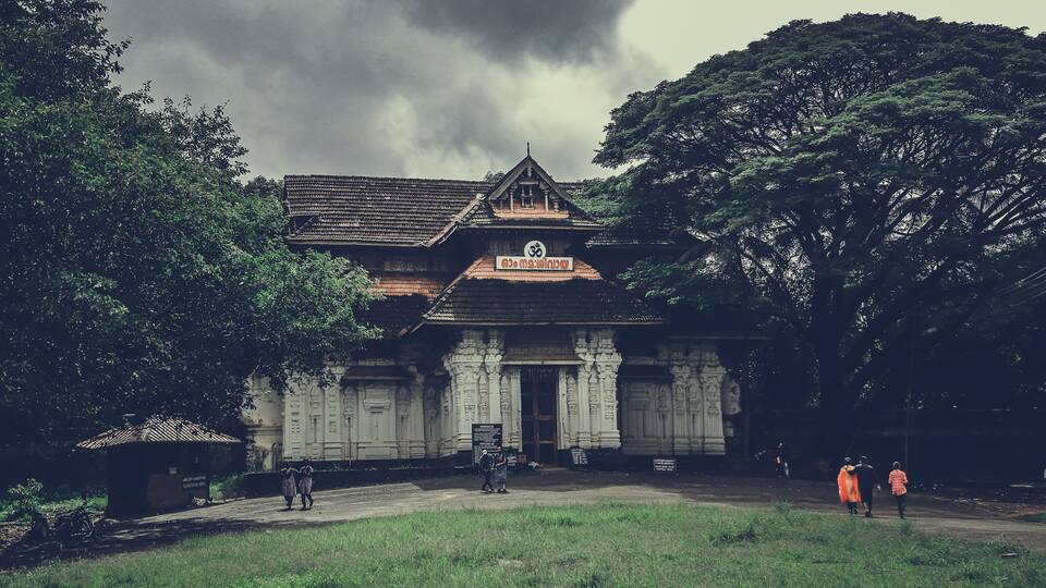 A traditional building with a tiled roof and ornate columns, surrounded by lush greenery.