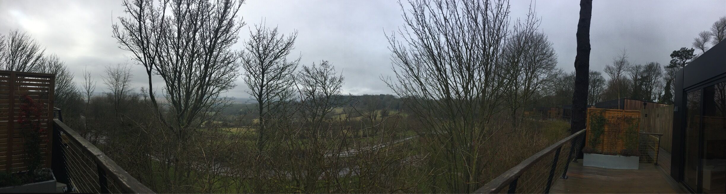 A balcony overlooking a rural landscape with leafless trees and a distant view of a village.