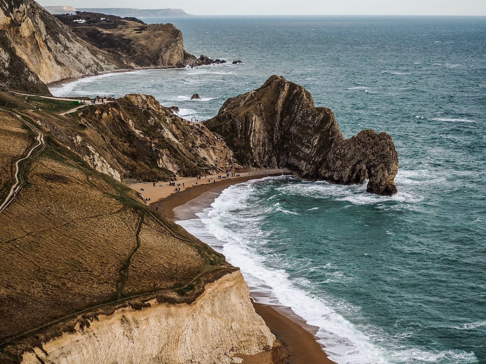 A coastal landscape with cliffs, a sandy beach, and the ocean.