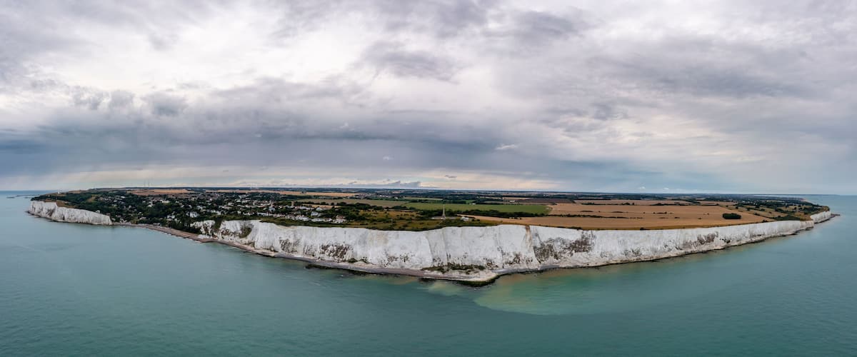 A coastal landscape with white cliffs, a small town, and a distant lighthouse.