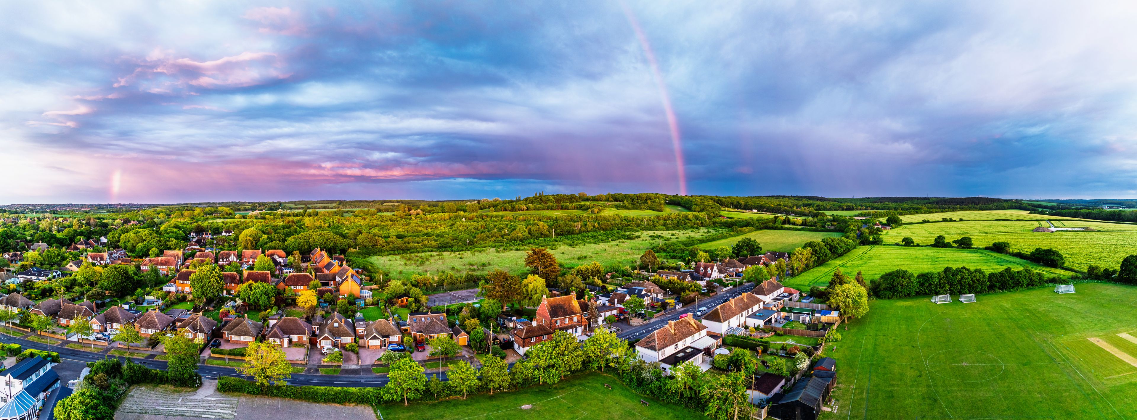 A rural village with houses, green fields, and a rainbow in the sky.