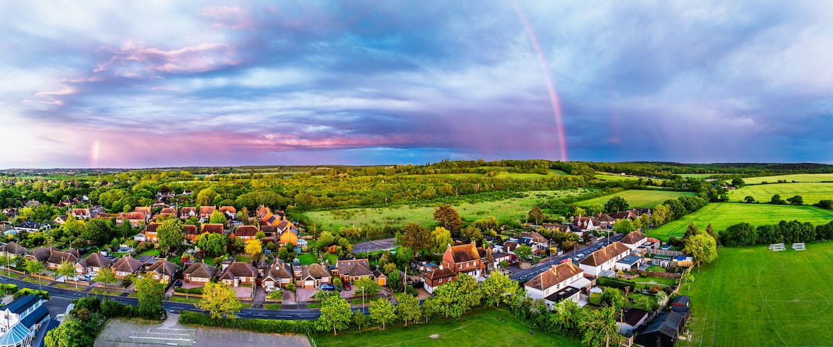 A rural village with houses, green fields, and a rainbow in the sky.