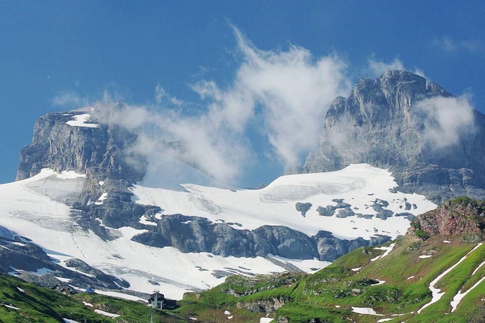 A snow-covered mountain with a prominent peak, a glacier, and green valleys.