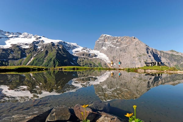 Ein Bergsee mit Spiegelungen, schneebedeckten Gipfeln und einem kleinen Holzbau.
