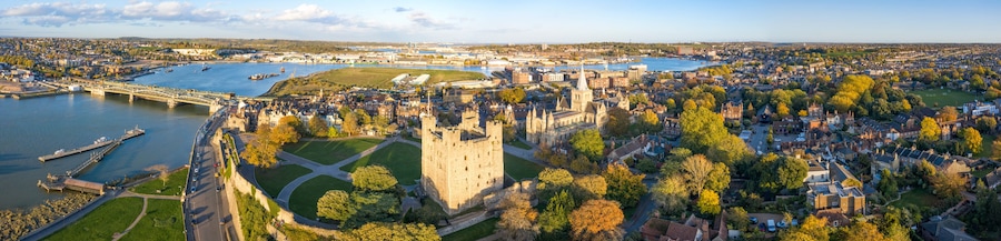 A panoramic view of a historic town with a prominent castle, a river, and surrounding greenery.