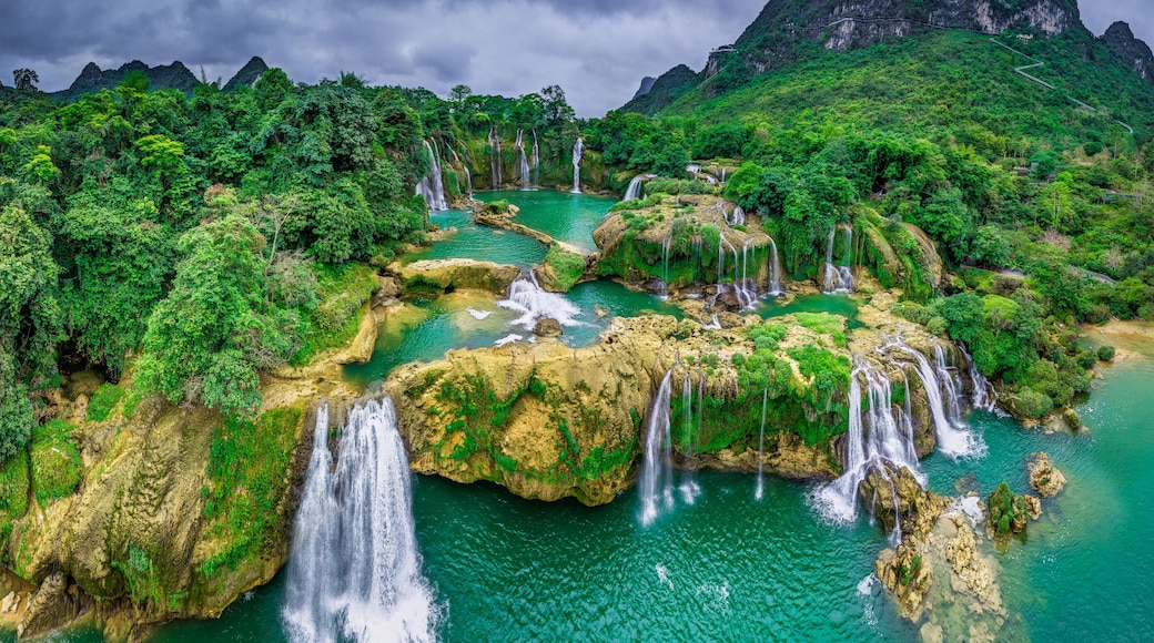 A series of waterfalls cascading into a turquoise pool surrounded by lush green forest and rocky terrain.
