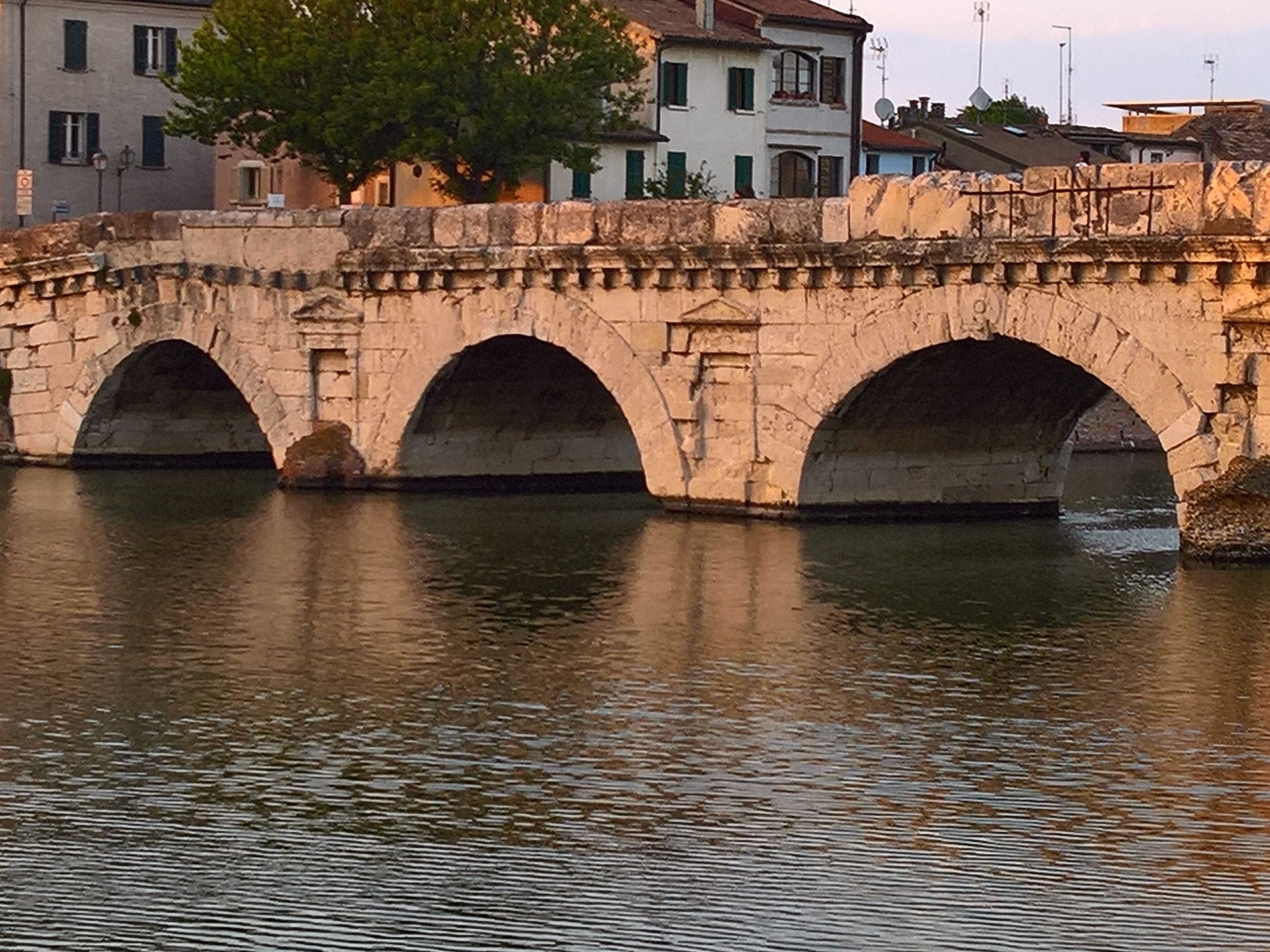 Un puente de piedra con tres arcos sobre una masa de agua, con edificios al fondo.