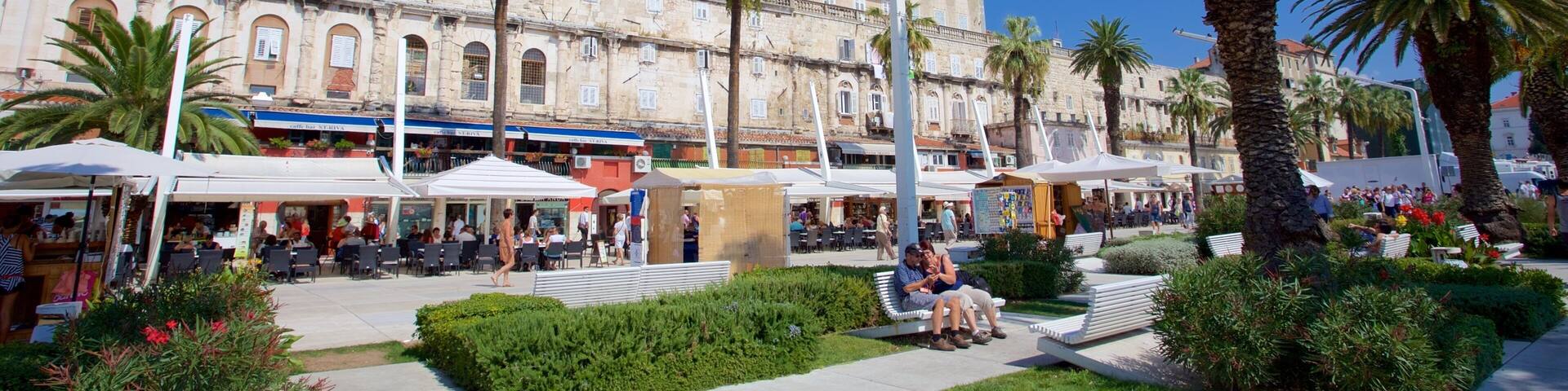 A sunny plaza with palm trees, outdoor cafes, and historic buildings.