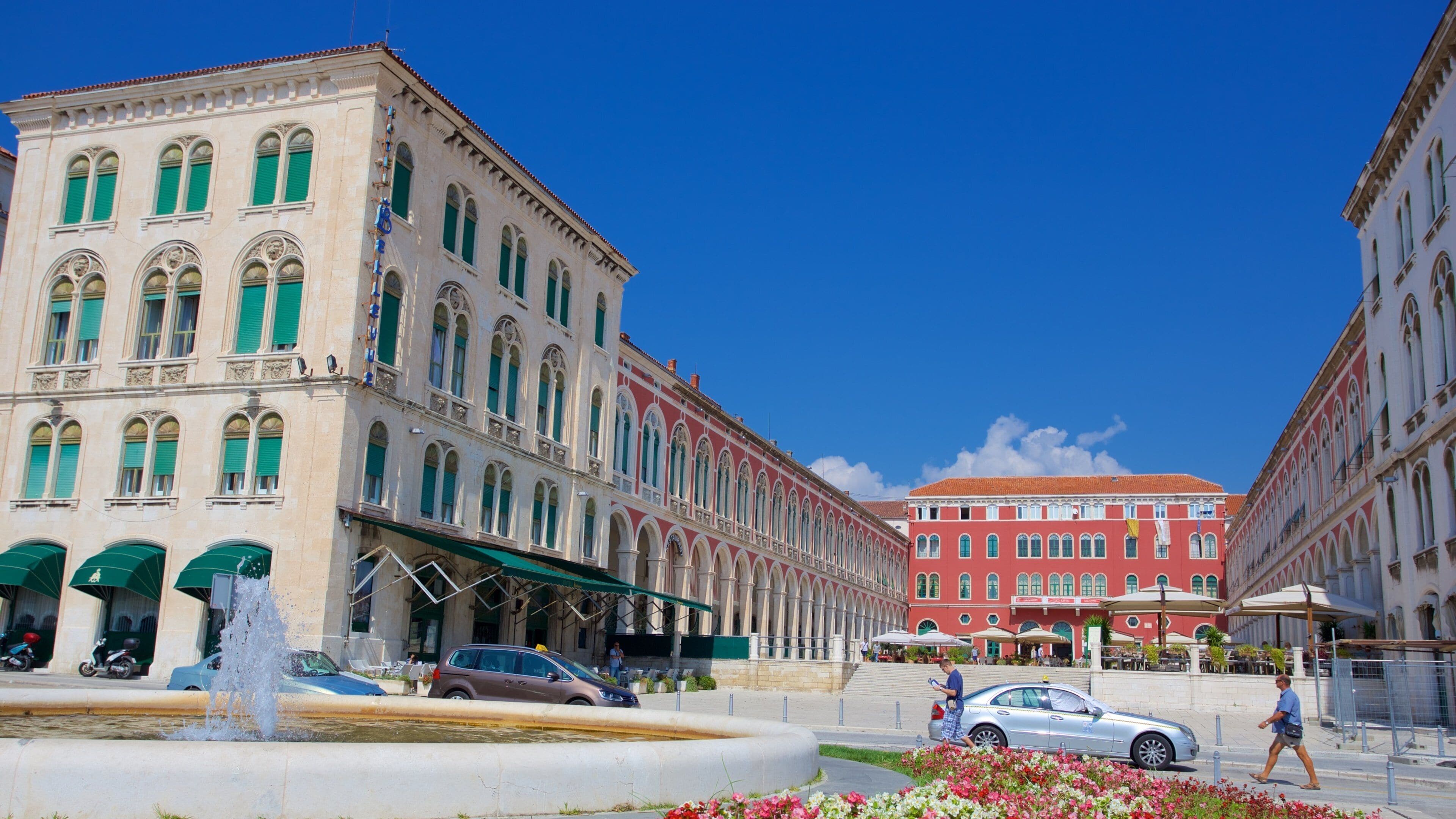 A historic square with ornate buildings, a fountain, and a pedestrian walkway.