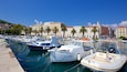 A marina with several boats docked, palm trees lining the waterfront, and historic buildings in the background.