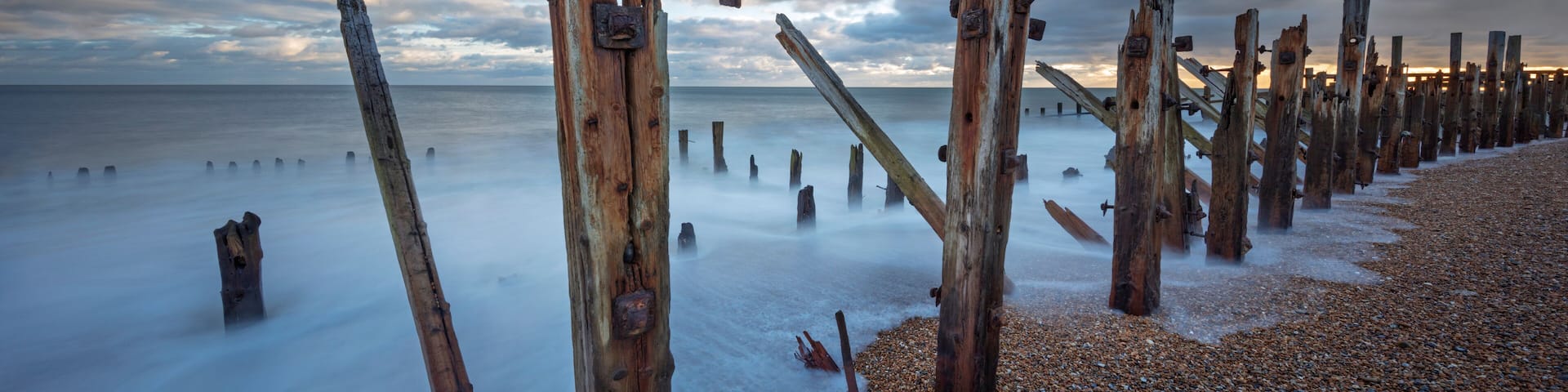 A beach with wooden posts and pebbles.