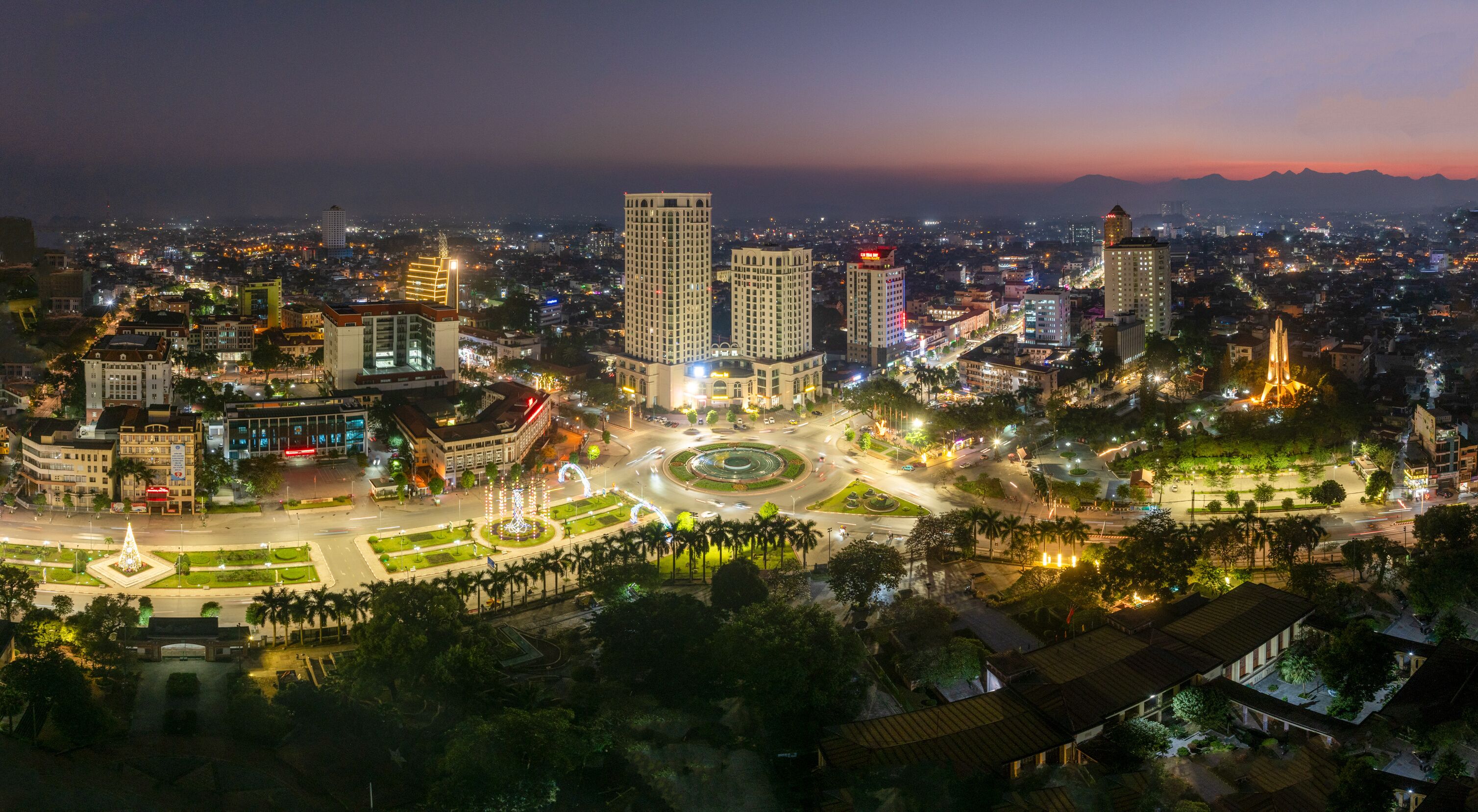 Aerial night views of a brightly illuminated central roundabout and surrounding cityscape in Thai Nguyen city, with traffic light trails.