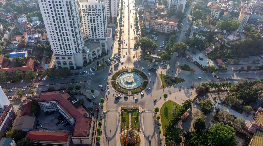 Backlit aerial view of Thai Nguyen city's central roundabout, with long shadows and sun glare, showcasing urban life under bright sunlight.