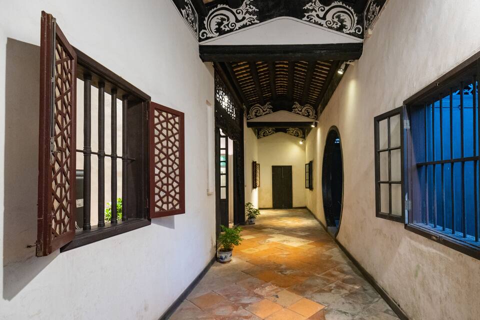 A narrow corridor with tiled flooring, wooden doors with lattice designs, and blue-tinted windows.
