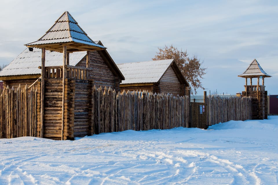 A wooden log cabin with a snow-covered roof and a wooden fence.