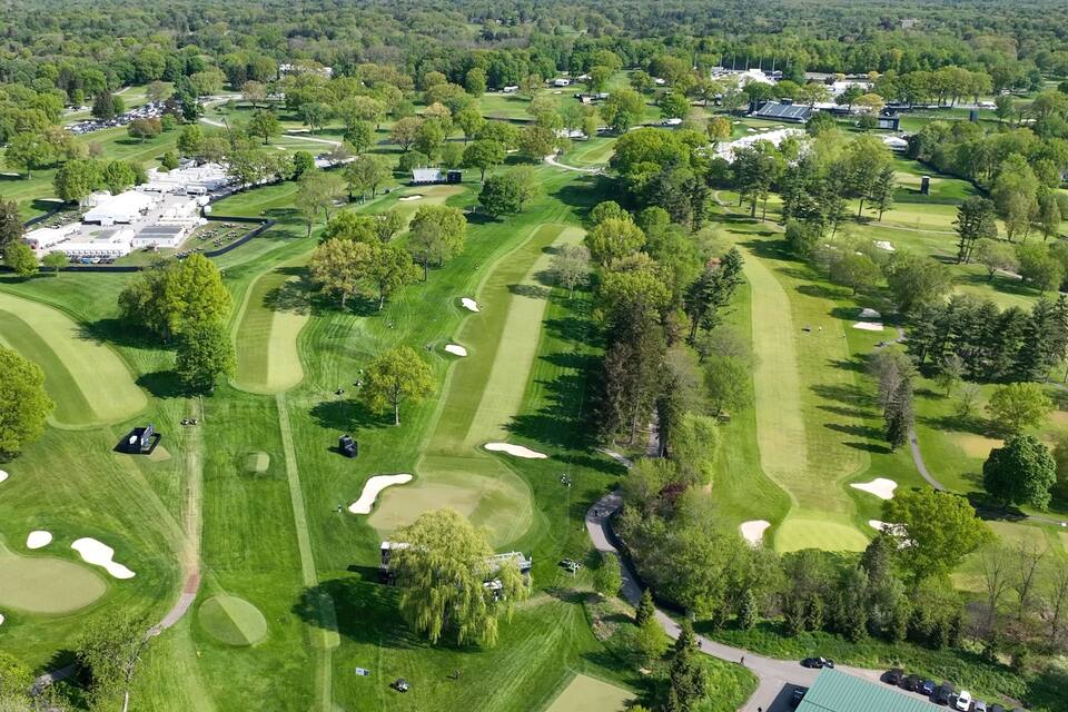 An aerial view of a golf course with multiple greens, sand bunkers, and a parking area.