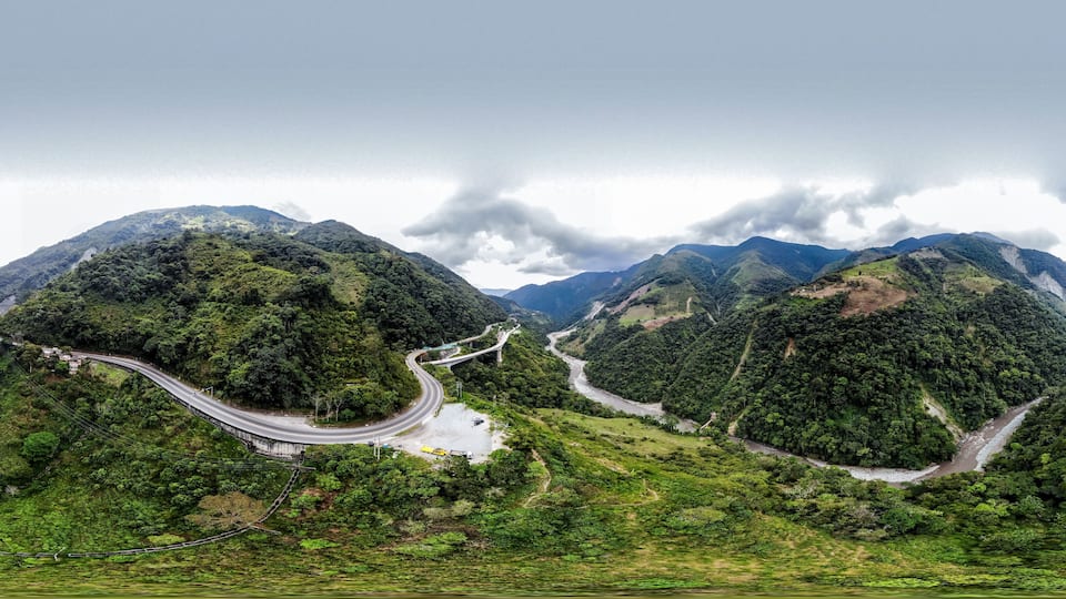 A winding mountain road surrounded by lush green hills and a river.
