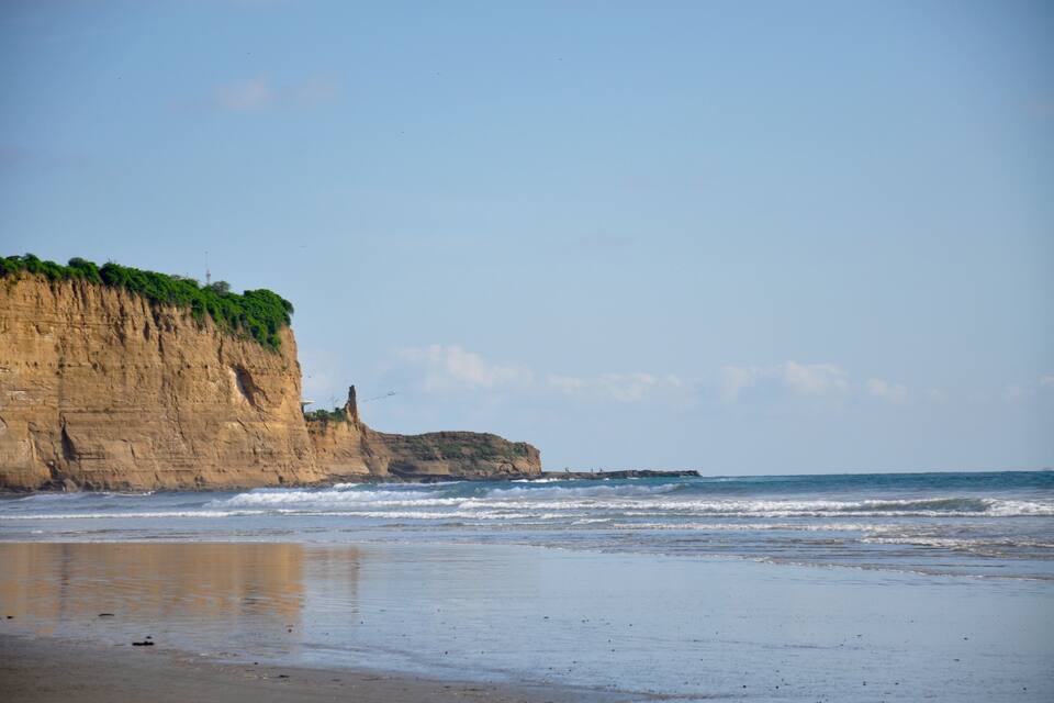 A beach with a large cliff and ocean waves.