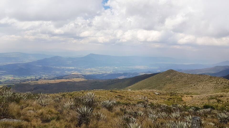A mountainous landscape with a valley in the distance, featuring rolling hills and sparse vegetation.
