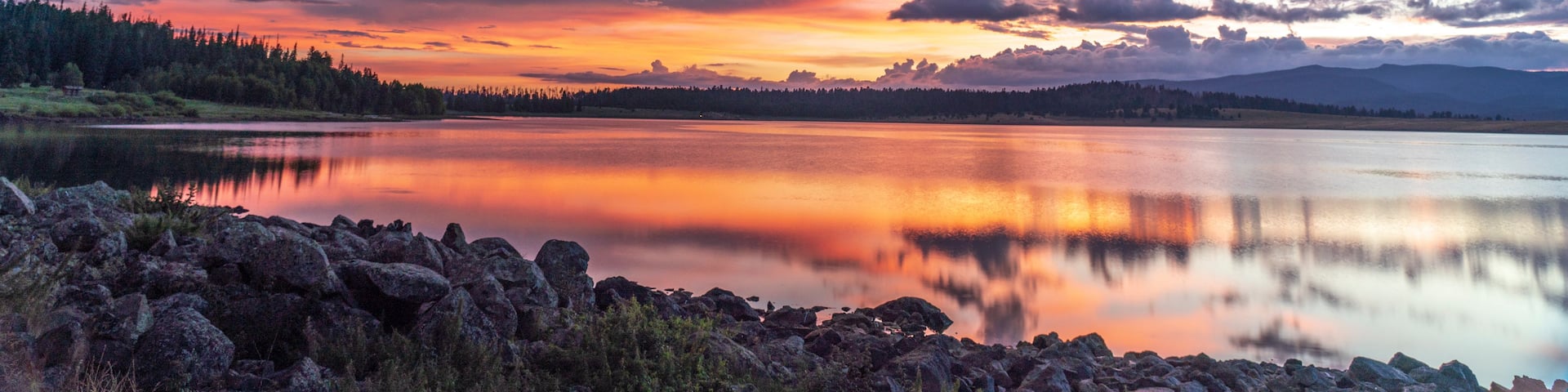 A calm lake reflecting a colorful sunset sky with mountains in the distance.