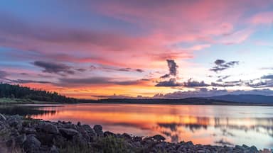 Un lago tranquilo refleja un cielo de atardecer colorido con montañas al fondo.